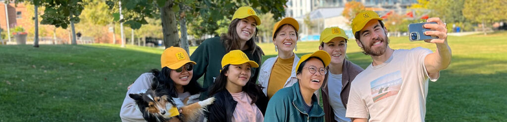 Happy team of dogwalkers with yellow waggr caps take laughing selfie at Regent Park